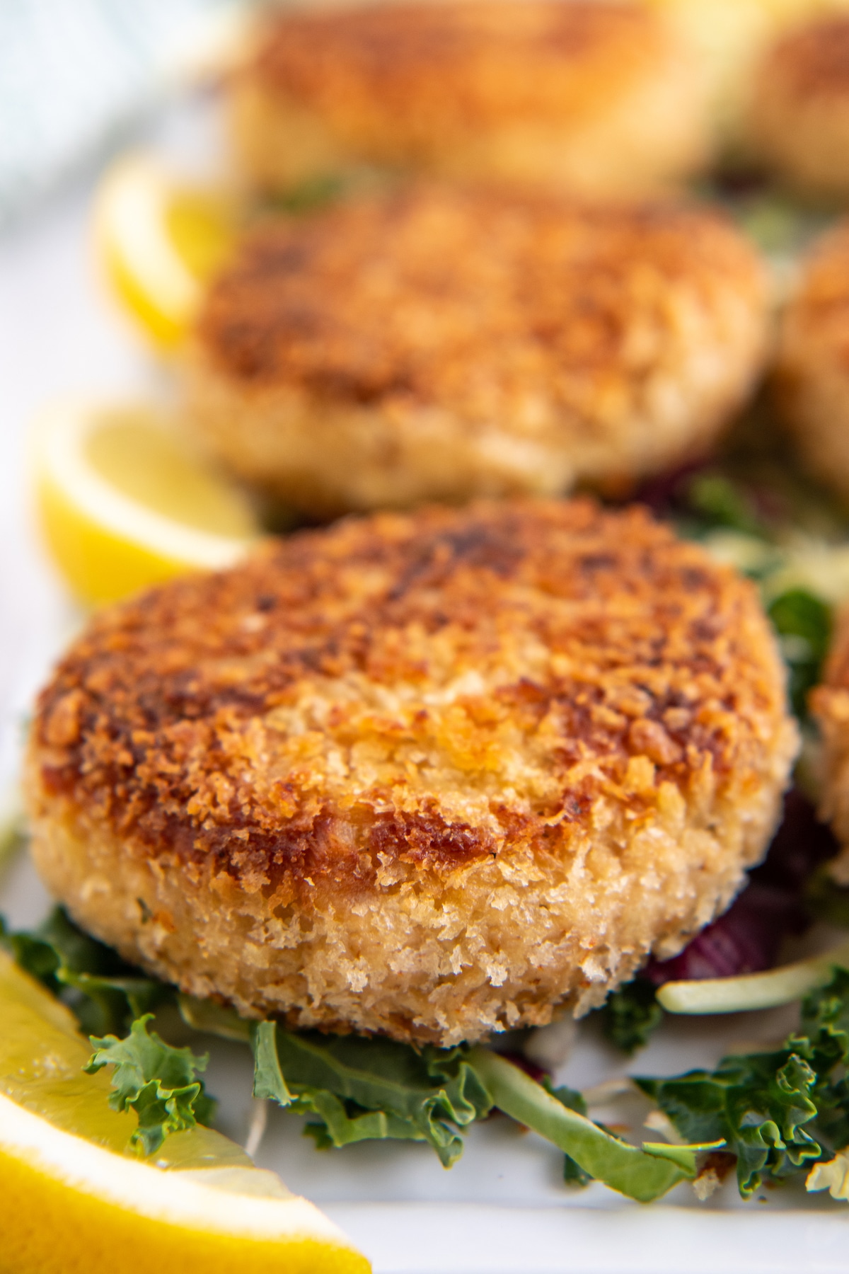 Tuna patties on a bed of greens with lemon wedges.