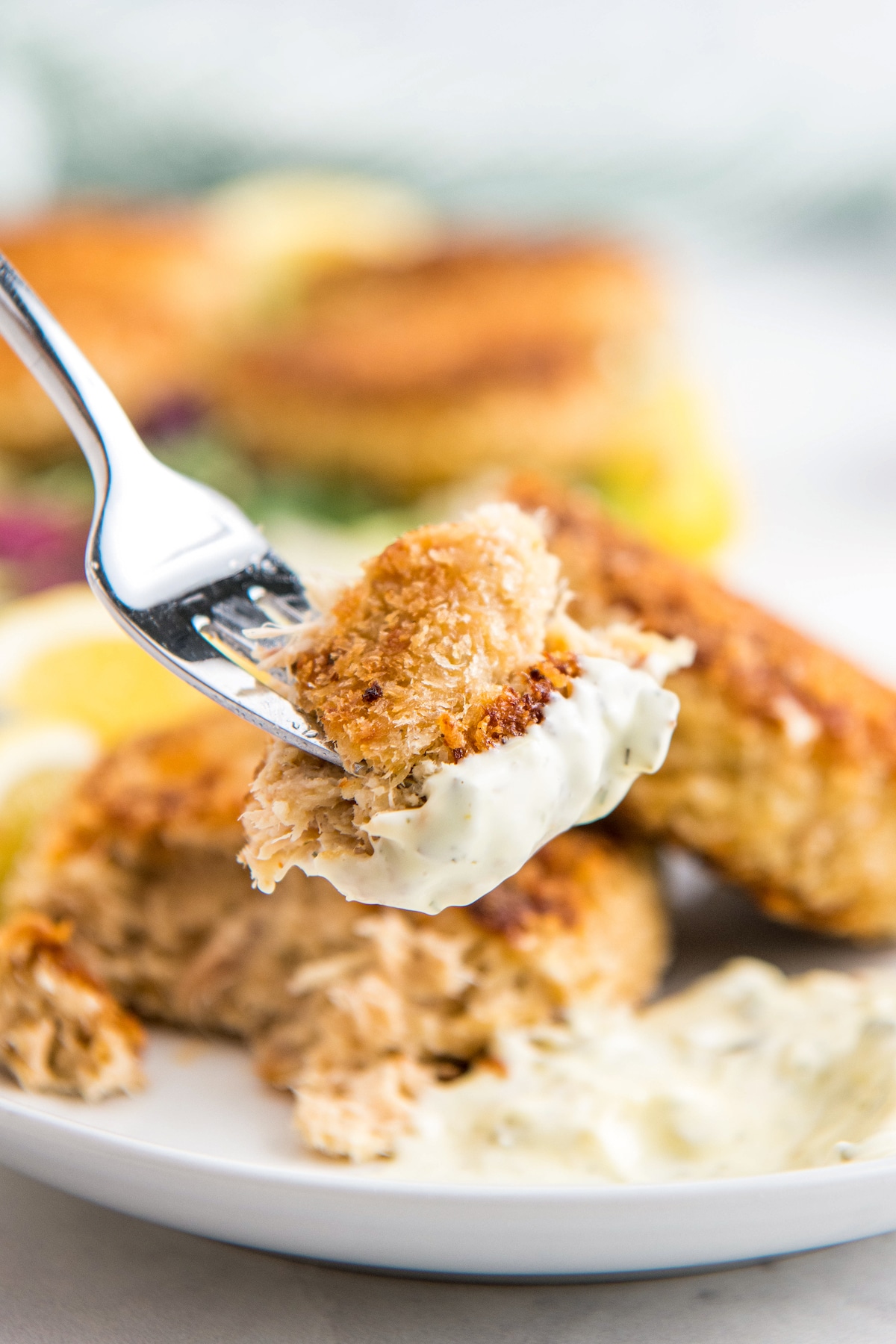 A bite of tuna cake on a fork with tartar sauce on it.