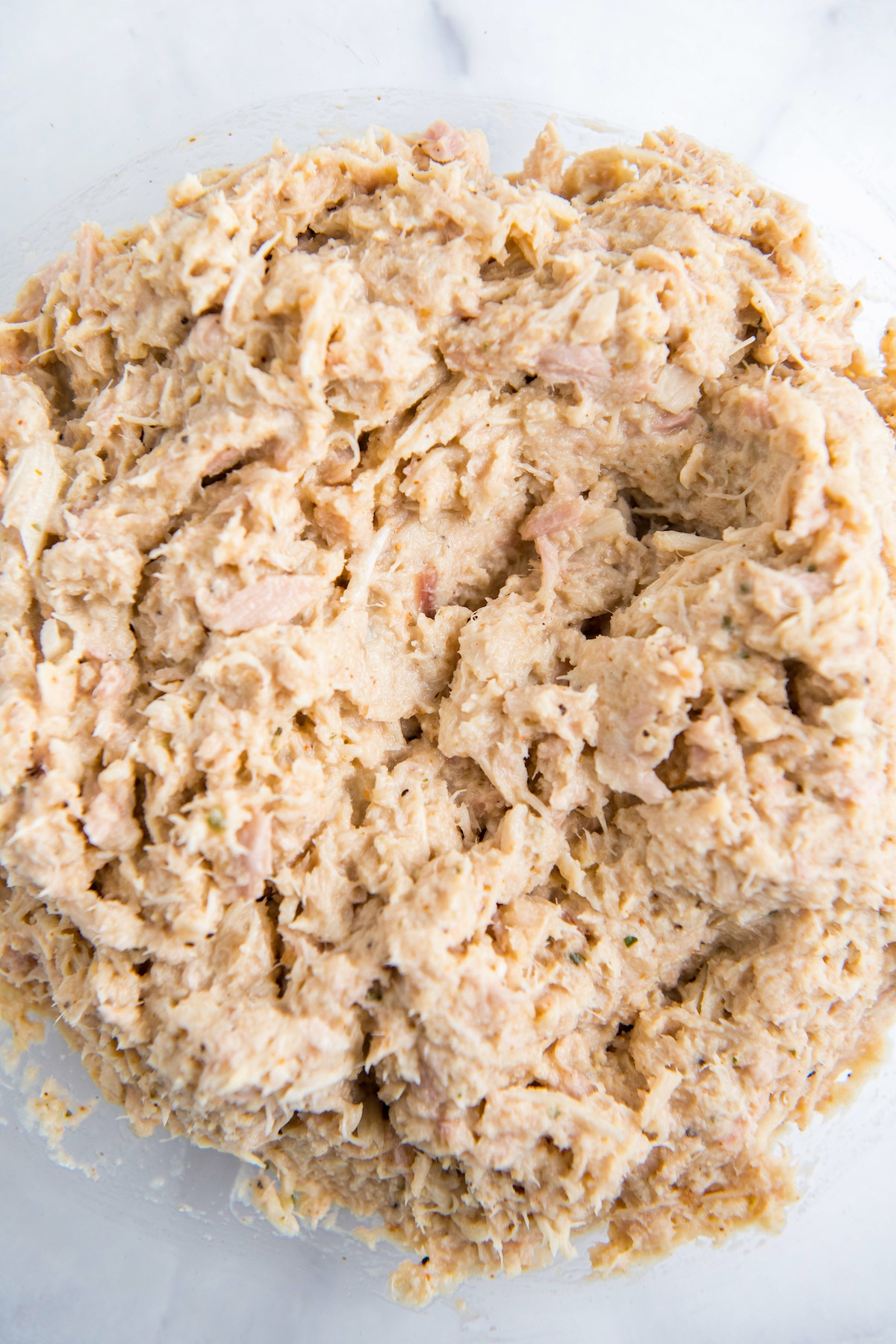 Tuna, mayo, seasonings and egg mixed together in a glass bowl.