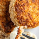 Tuan patties on a white plate with a fork dipping a bite in tartar sauce.