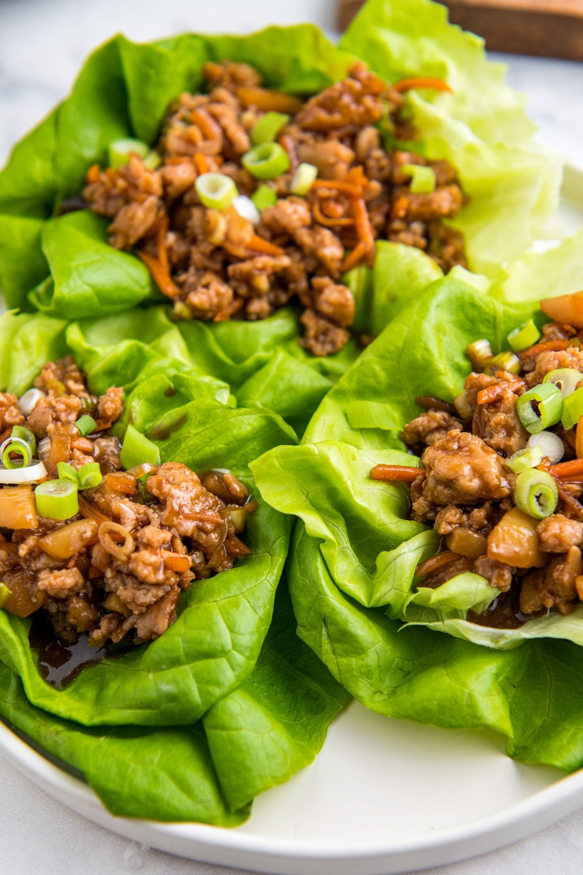 Three chicken lettuce wraps on a white plate.