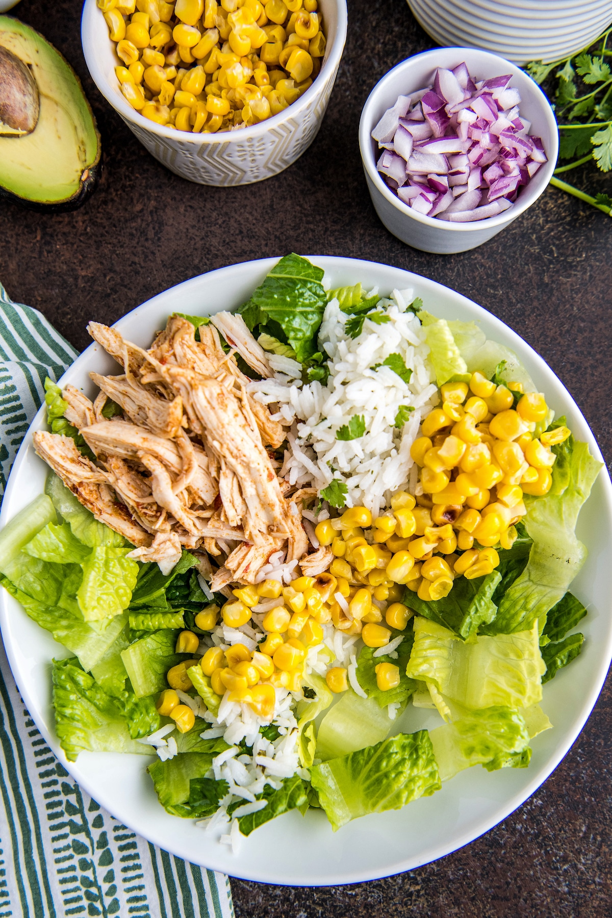 A white bowl filled with lettuce, rice, corn and chicken.
