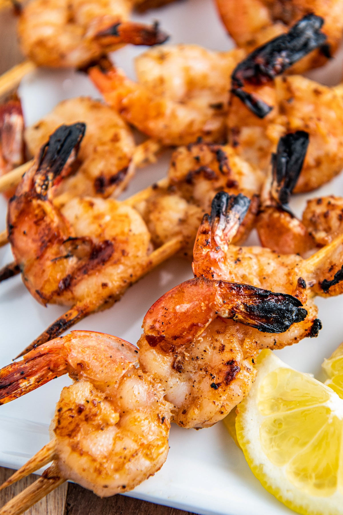 Grilled shrimp on skewers on a white plate with lemon.
