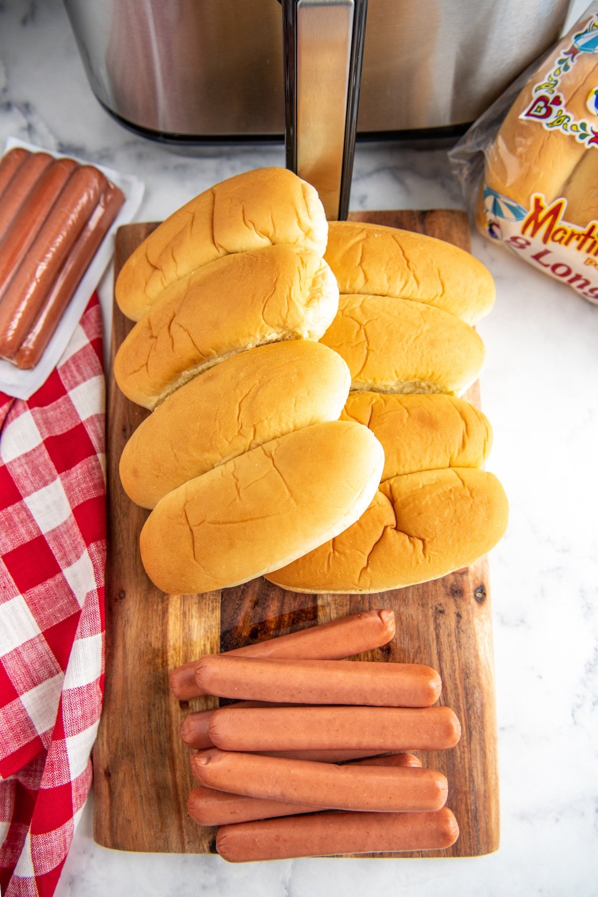Hot dogs and buns on a cutting board with air fryer in background.