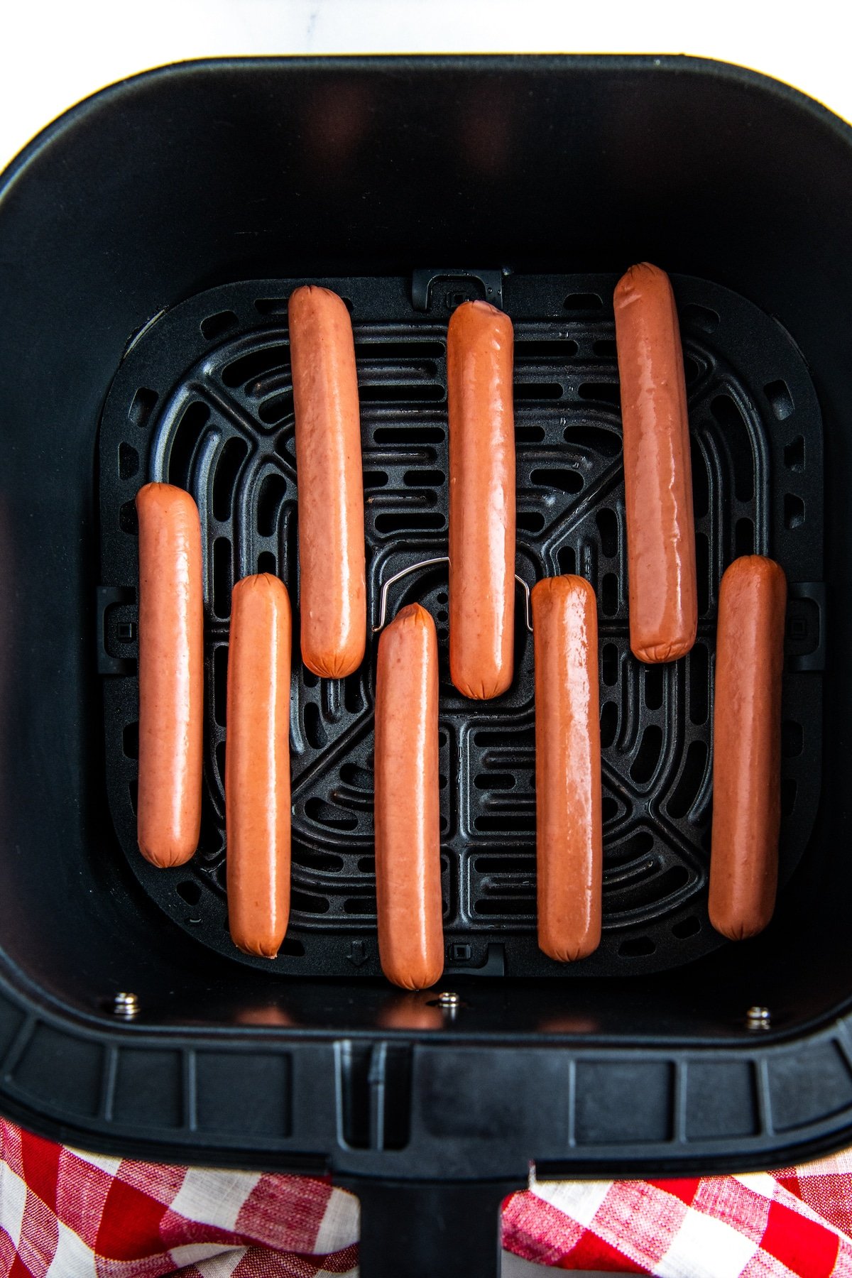 Uncooked hot dogs in air fryer basket.