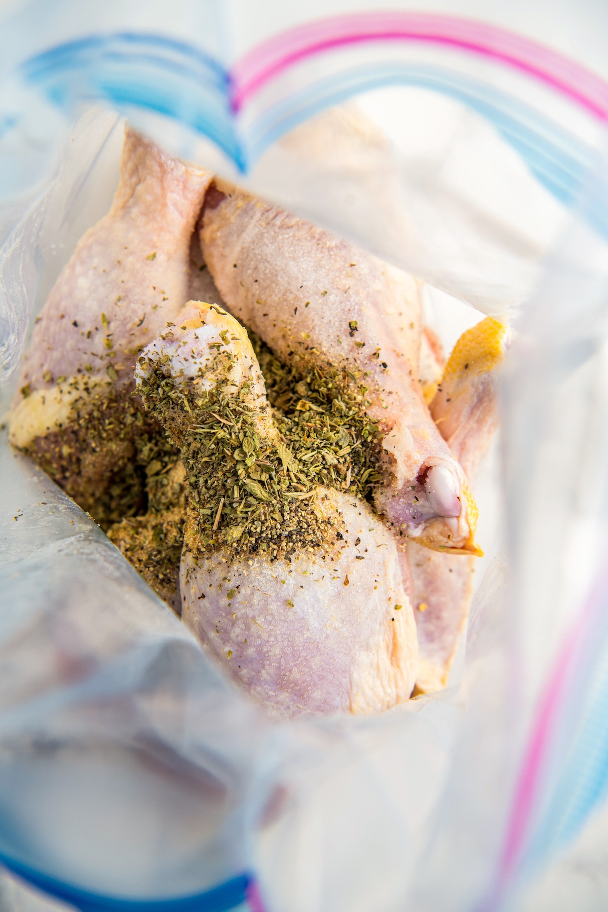 Raw chicken legs in a ziplock bag with seasonings poured on top.