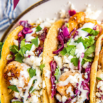 Two shrimp tacos with homemade slaw and toppings.