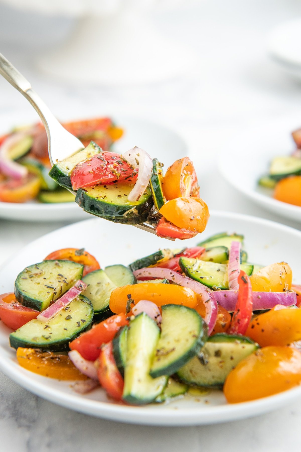 A fork picking up a bite of cucumber tomato salad from a plate.