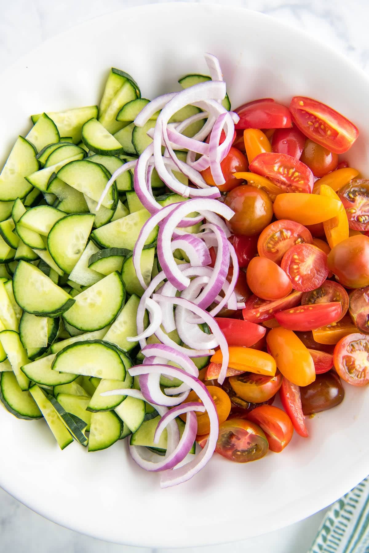 Cucumbers, onions and tomatoes lined up in a white bowl.