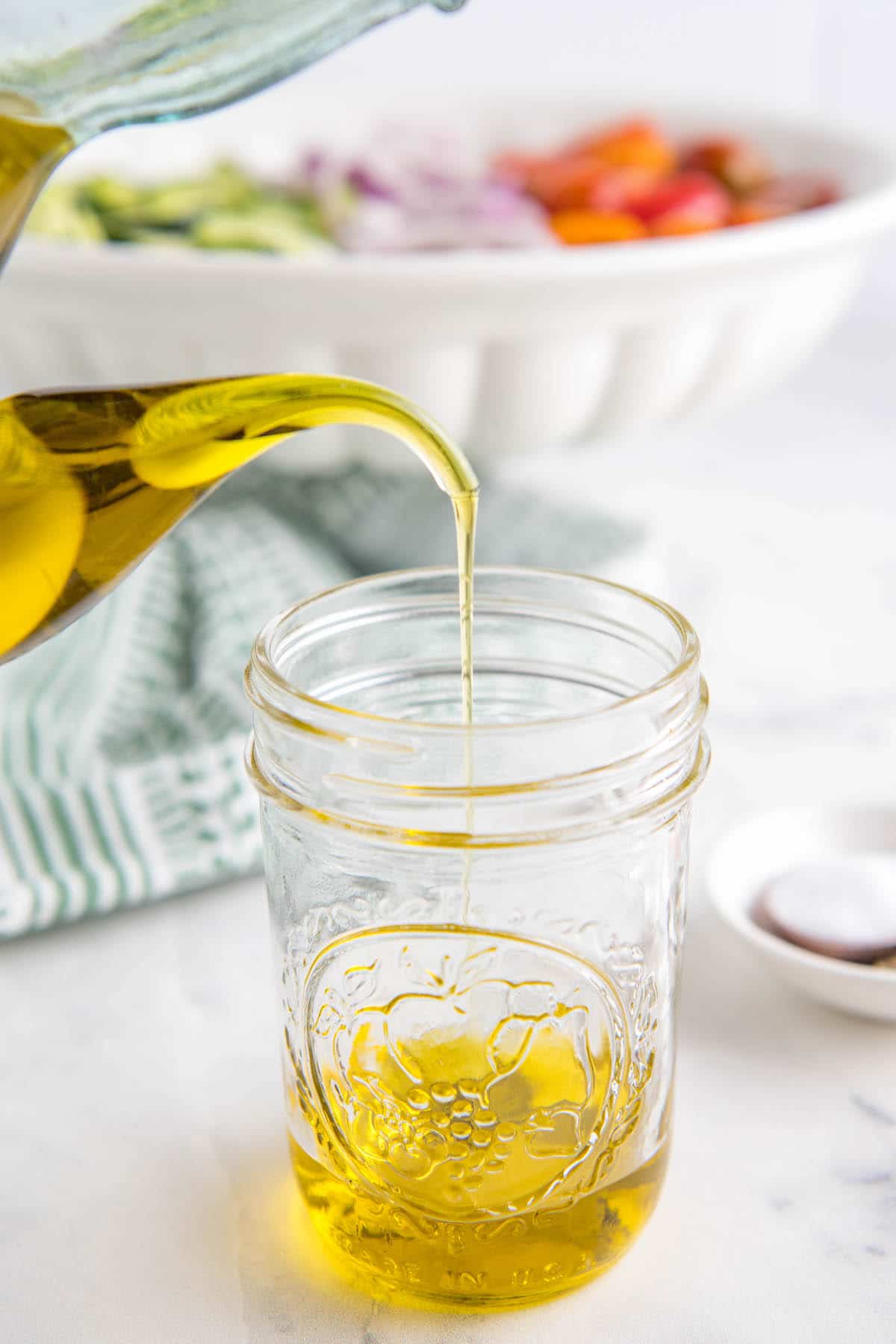 Olive oil being poured into a glass mason jar.