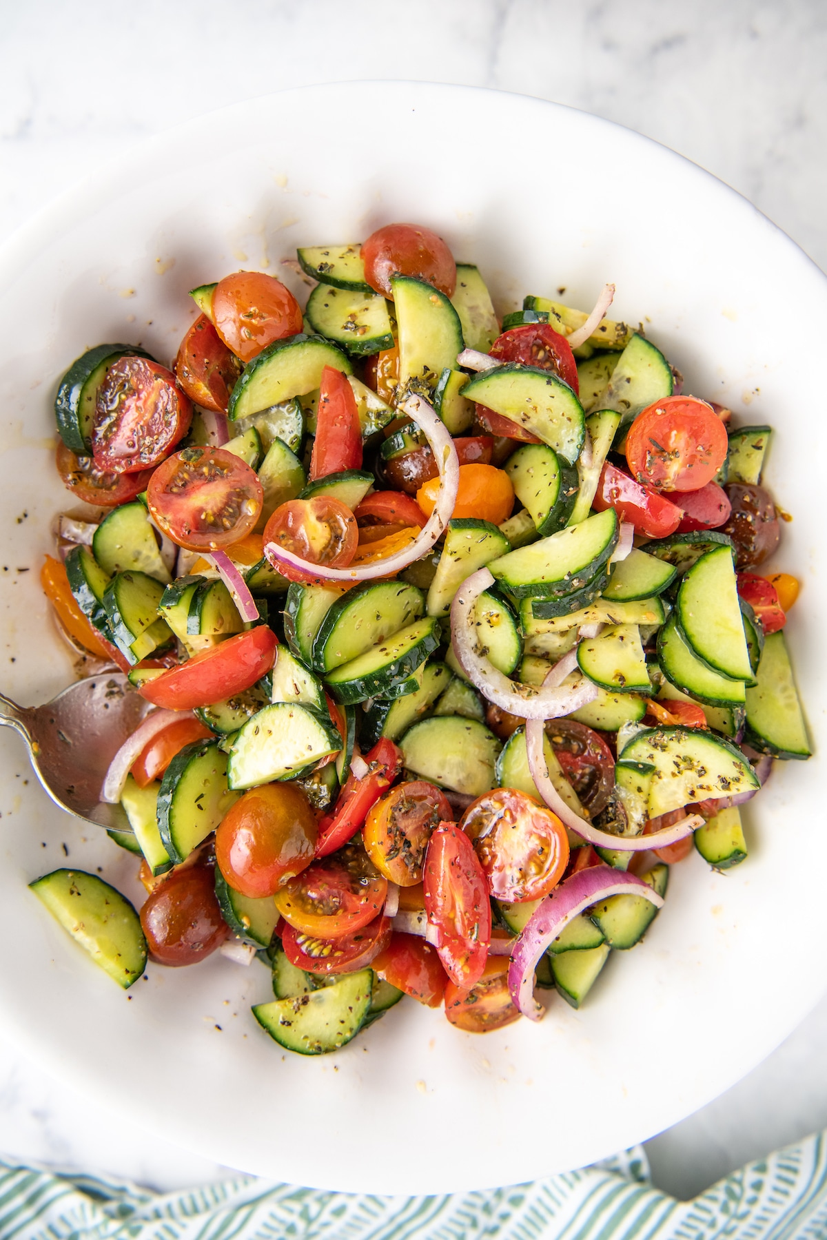 Cucumber tomato onion salad in a large white bowl with a spoon.