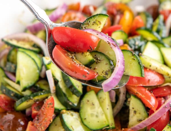 A spoon scooping up a serving of cucumber tomato salad.
