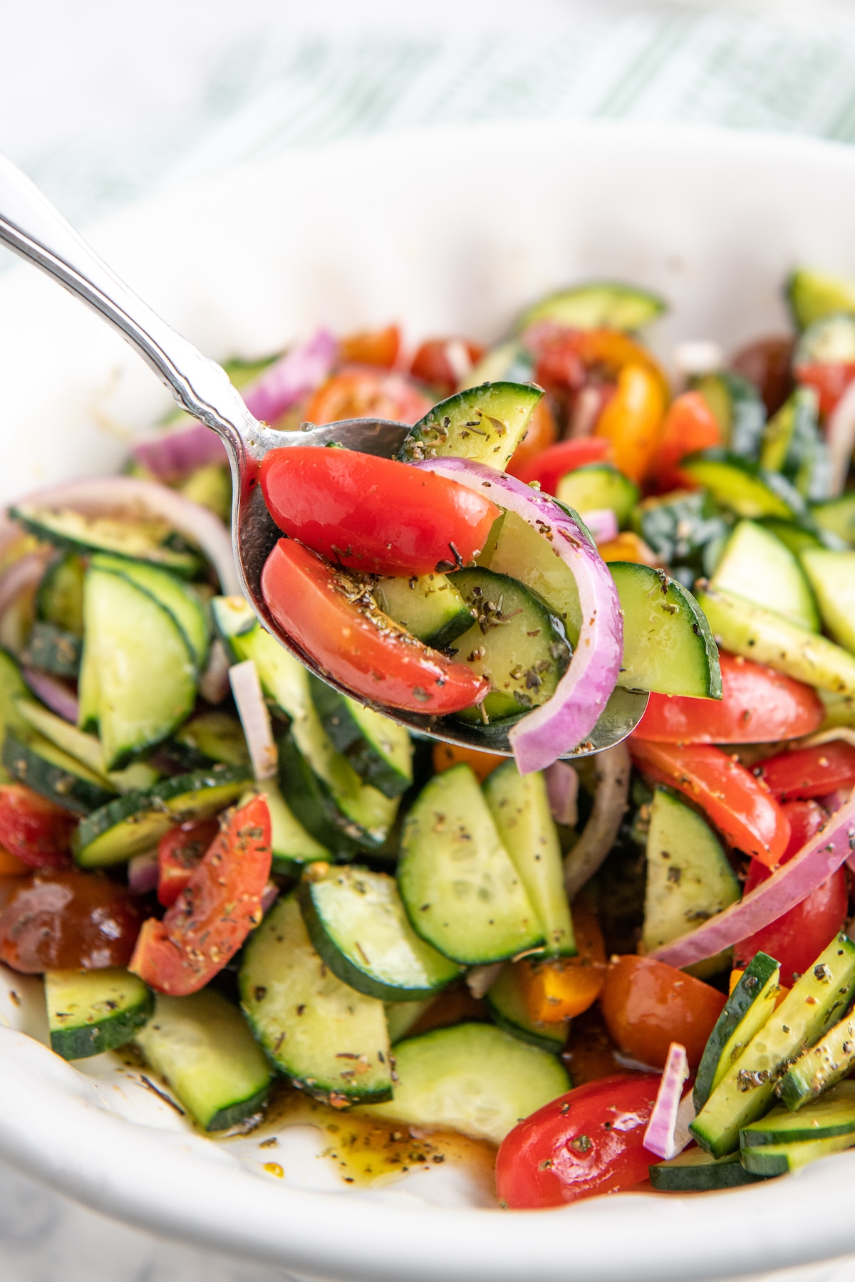 A spoon scooping up a serving of cucumber tomato salad.