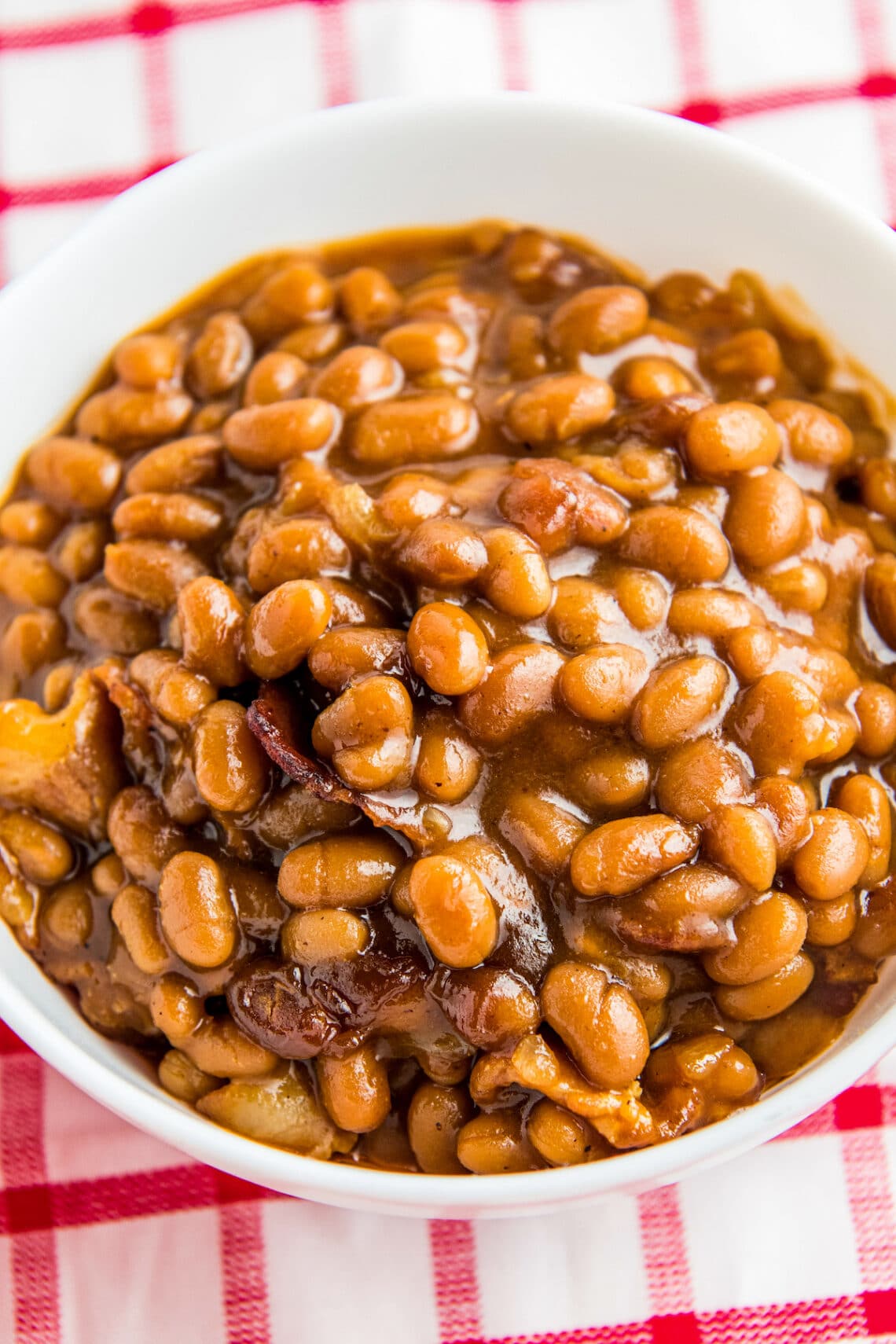 Baked beans in a white bowl on a picnic table.