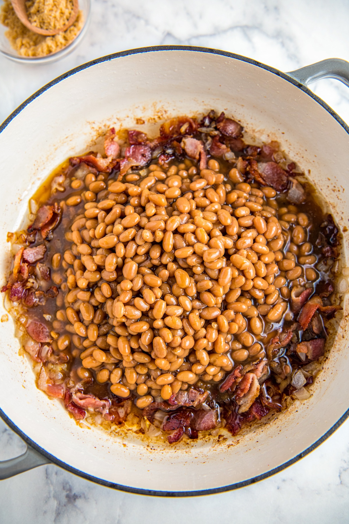 Beans added to a skillet with bacon and onion.