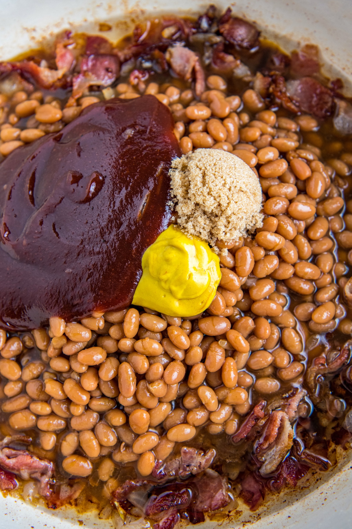 Brown sugar, mustard and bbq sauce added to a skillet with beans and sautéed bacon and onions.