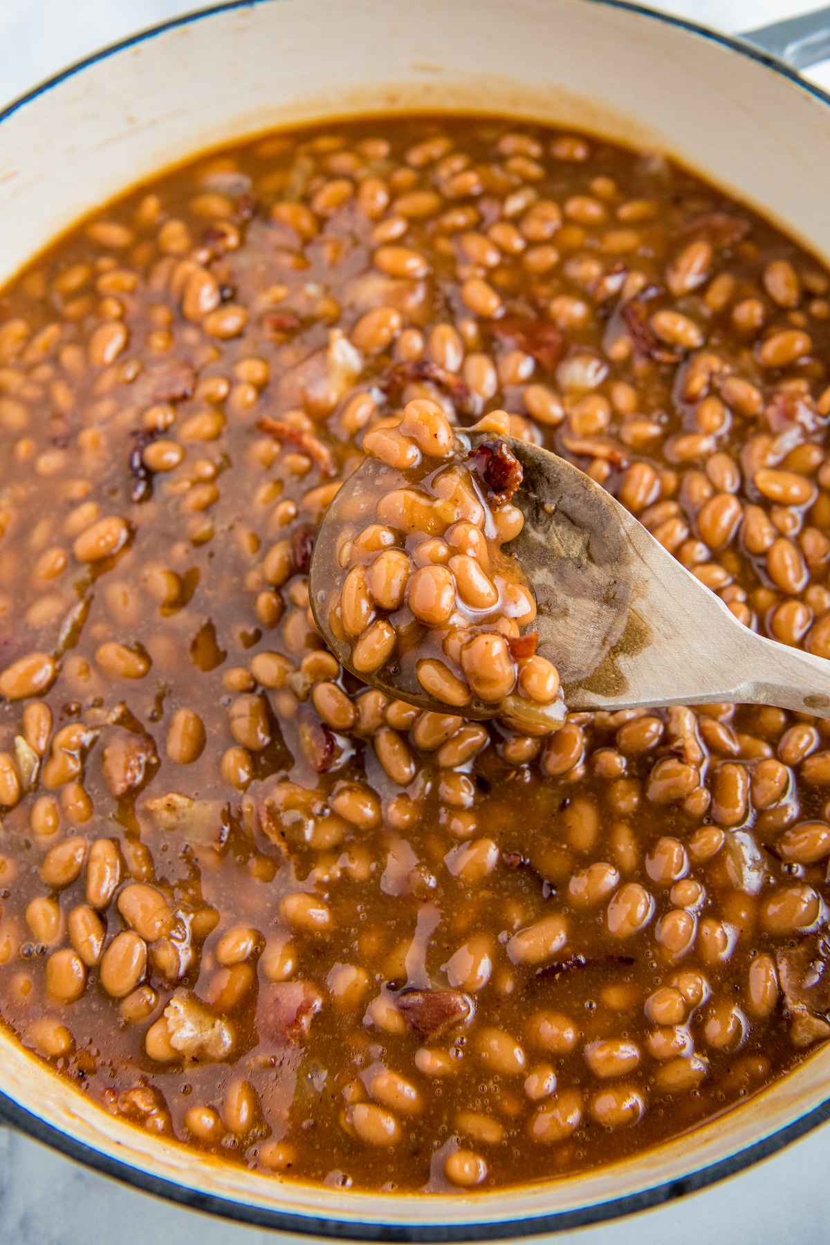 Beans in a skillet with a wooden spoon stirring and scooping some up.