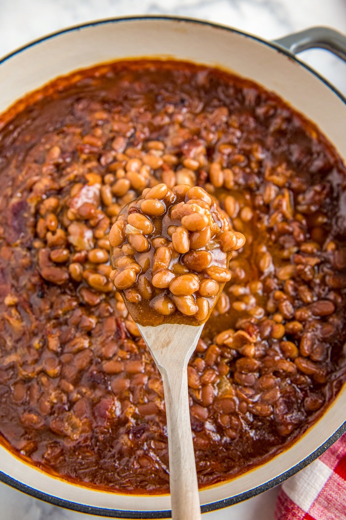 Baked Beans in a skillet with a wooden spoon scooping some up.