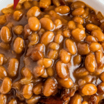 Up close image of baked beans with bacon in a white bowl.