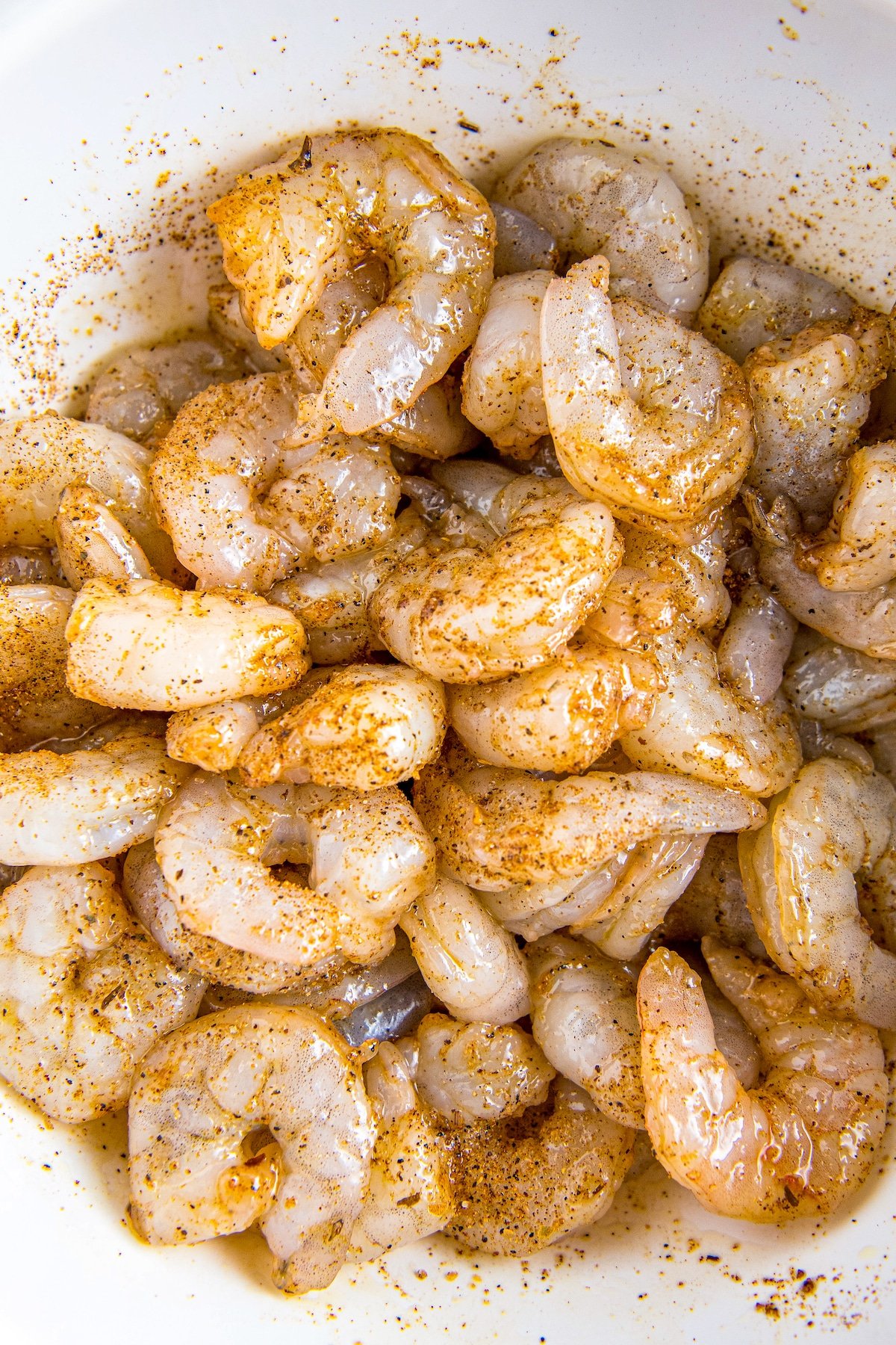 Raw shrimp tossed in cajun seasoning in a white bowl.