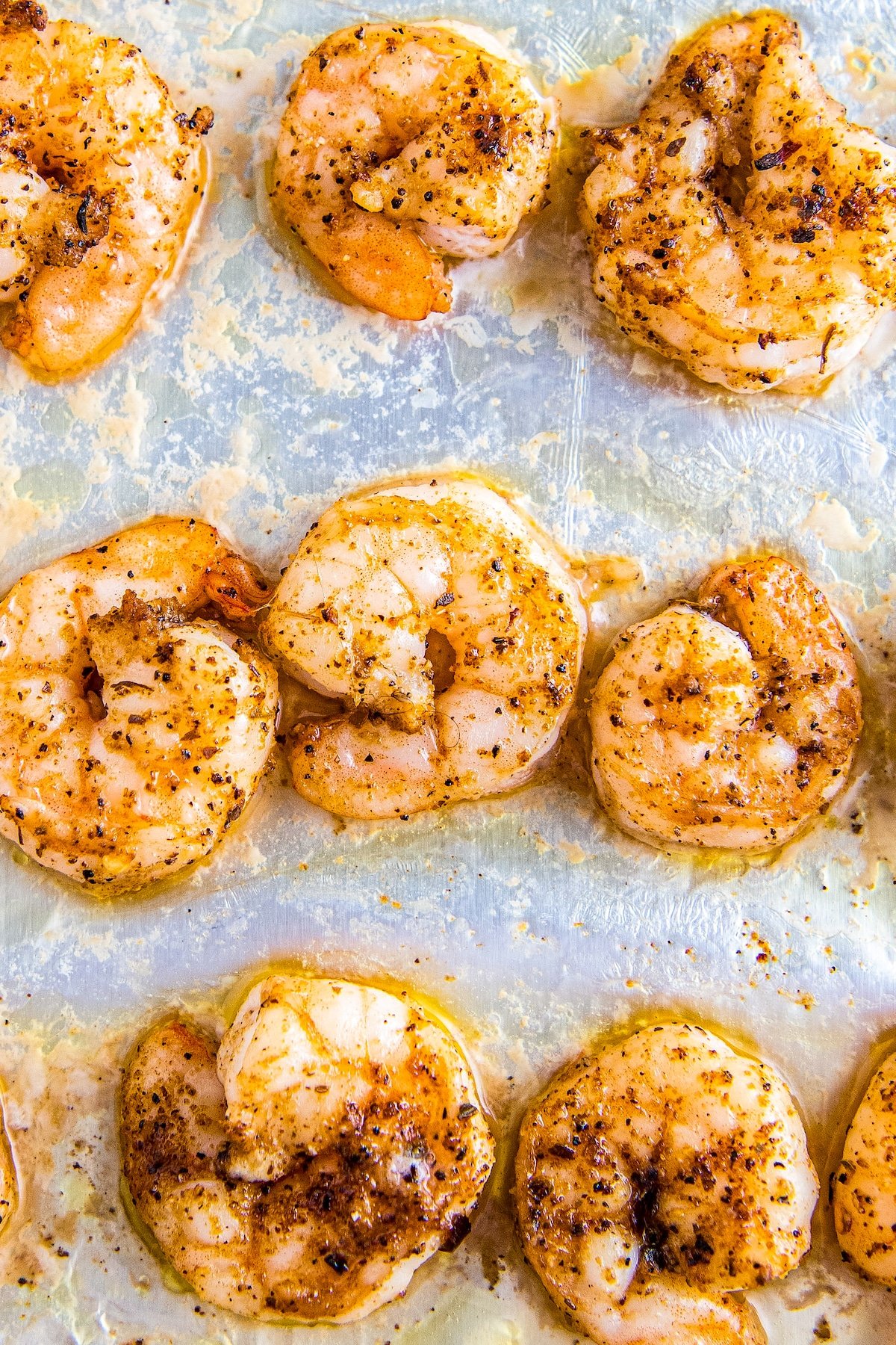 Cooked seasoned shrimp pan a baking sheet wrapped with foil.