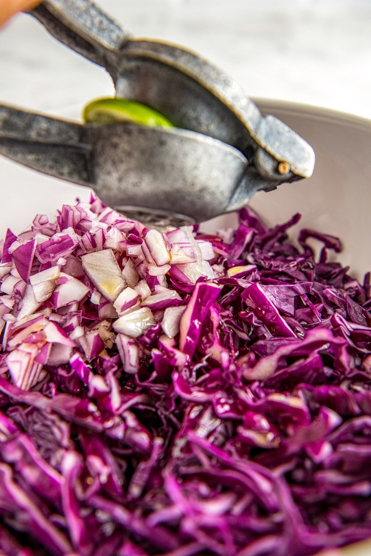 A white bowl filled with red cabbage, red onion and lime juice being squeezed in.