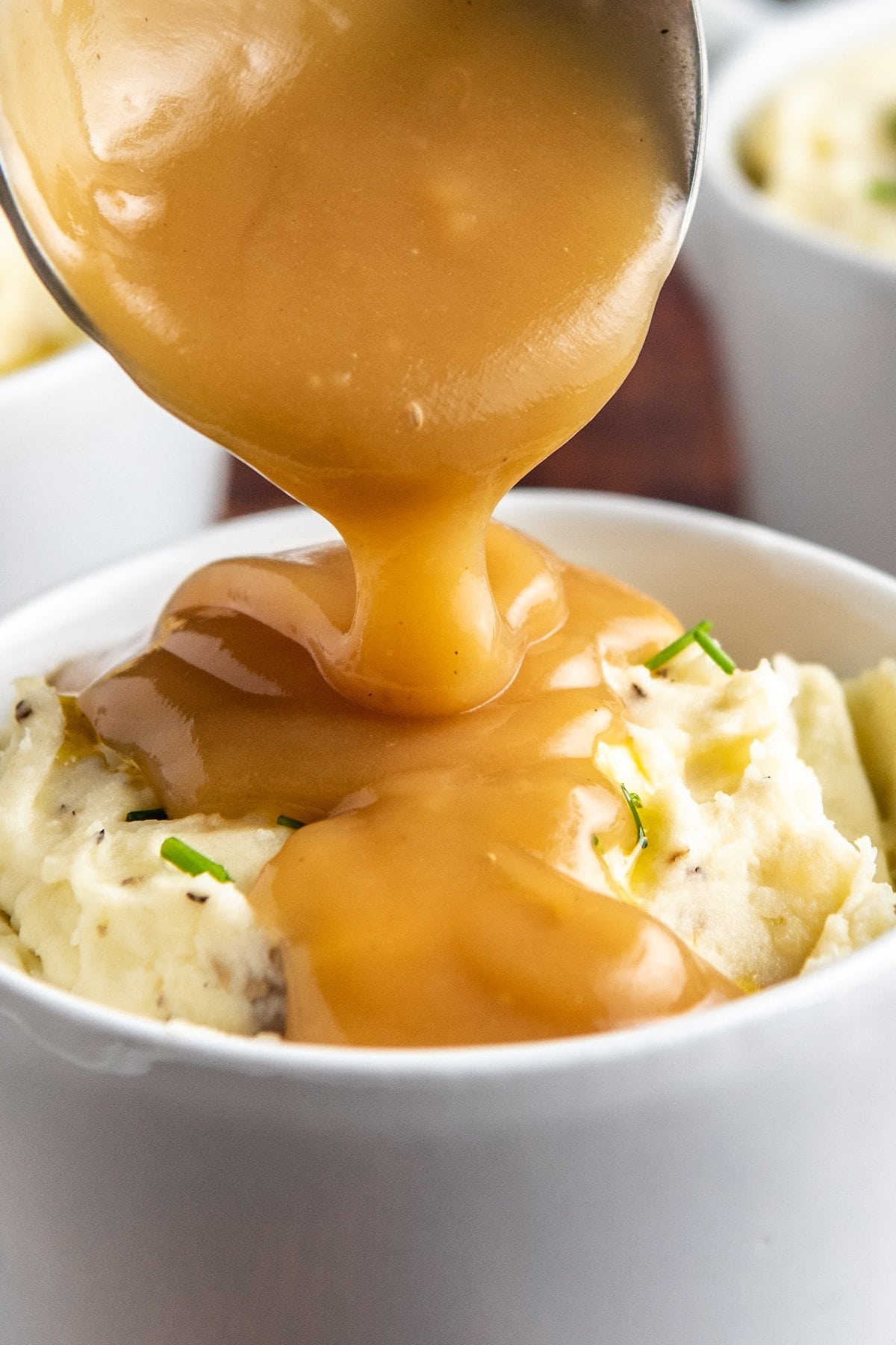 Gravy being poured on top of mashed potatoes in a bowl.