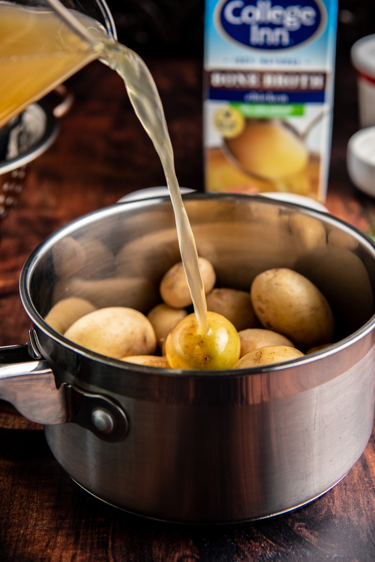 Chicken broth being poured into a skillet with potatoes.