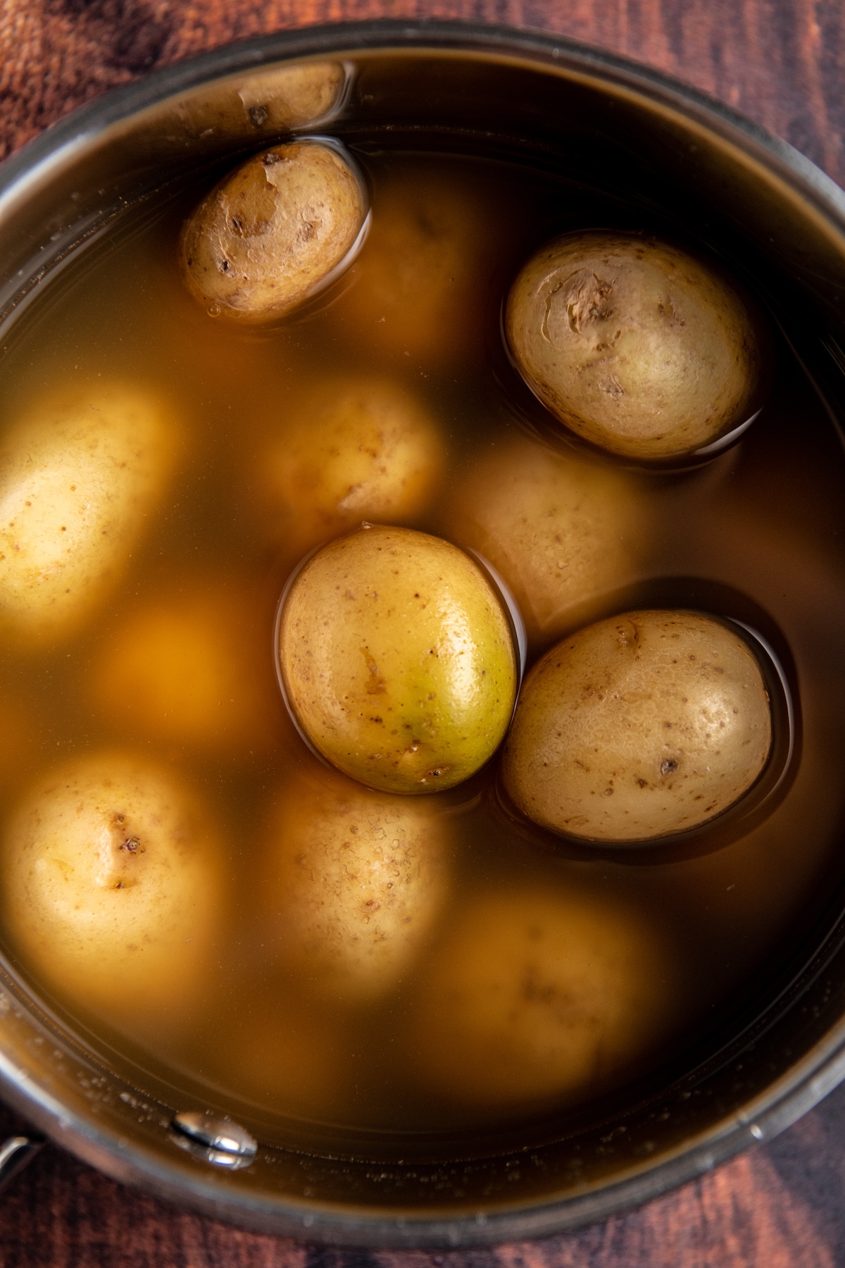 Small potatoes in chicken broth in a pot.
