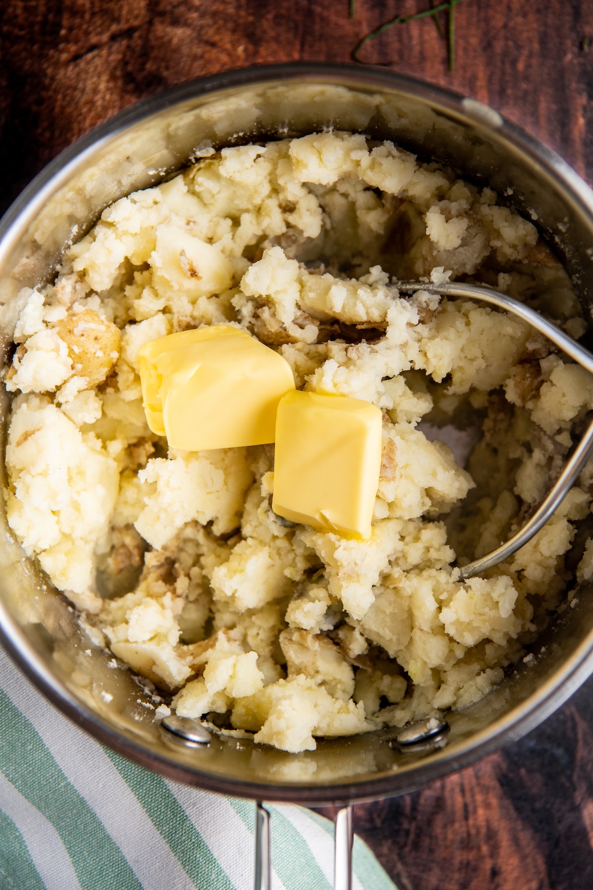 Butter being added to mashed potatoes in a pot.