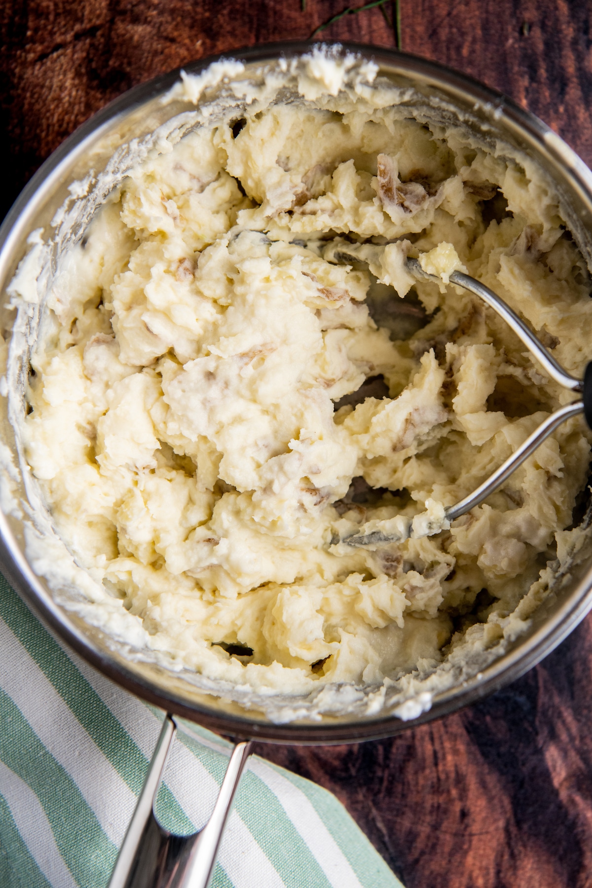 Potatoes being mashed with butter and sour cream in a pot.