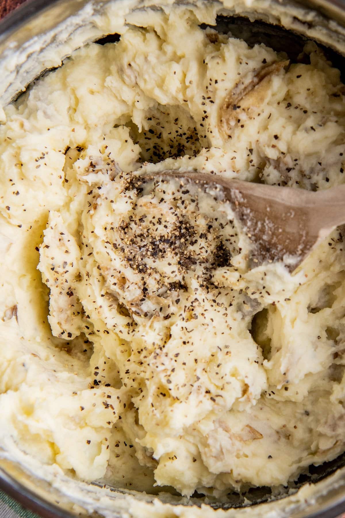 Salt and pepper added to mashed potatoes with a wooden spoon stirring them.
