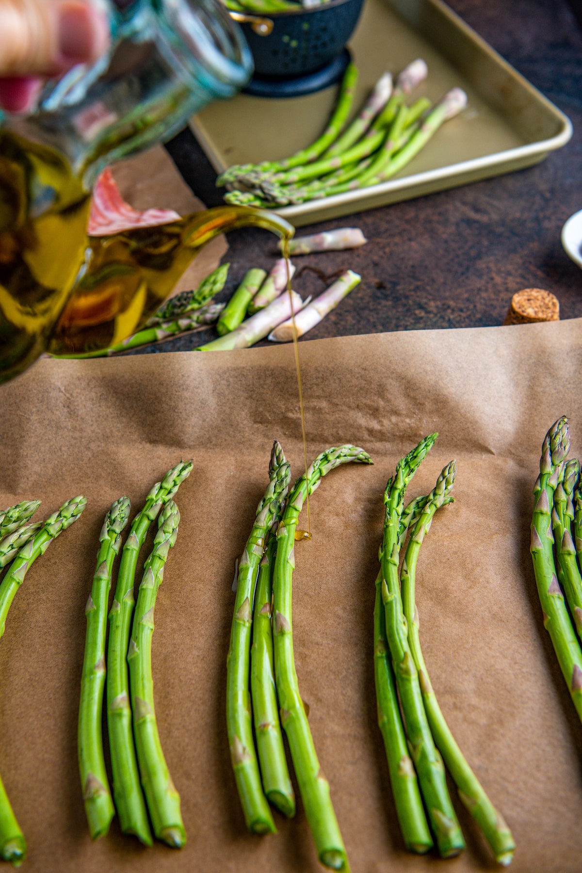 Asparagus on parchment paper being drizzled with olive oil.