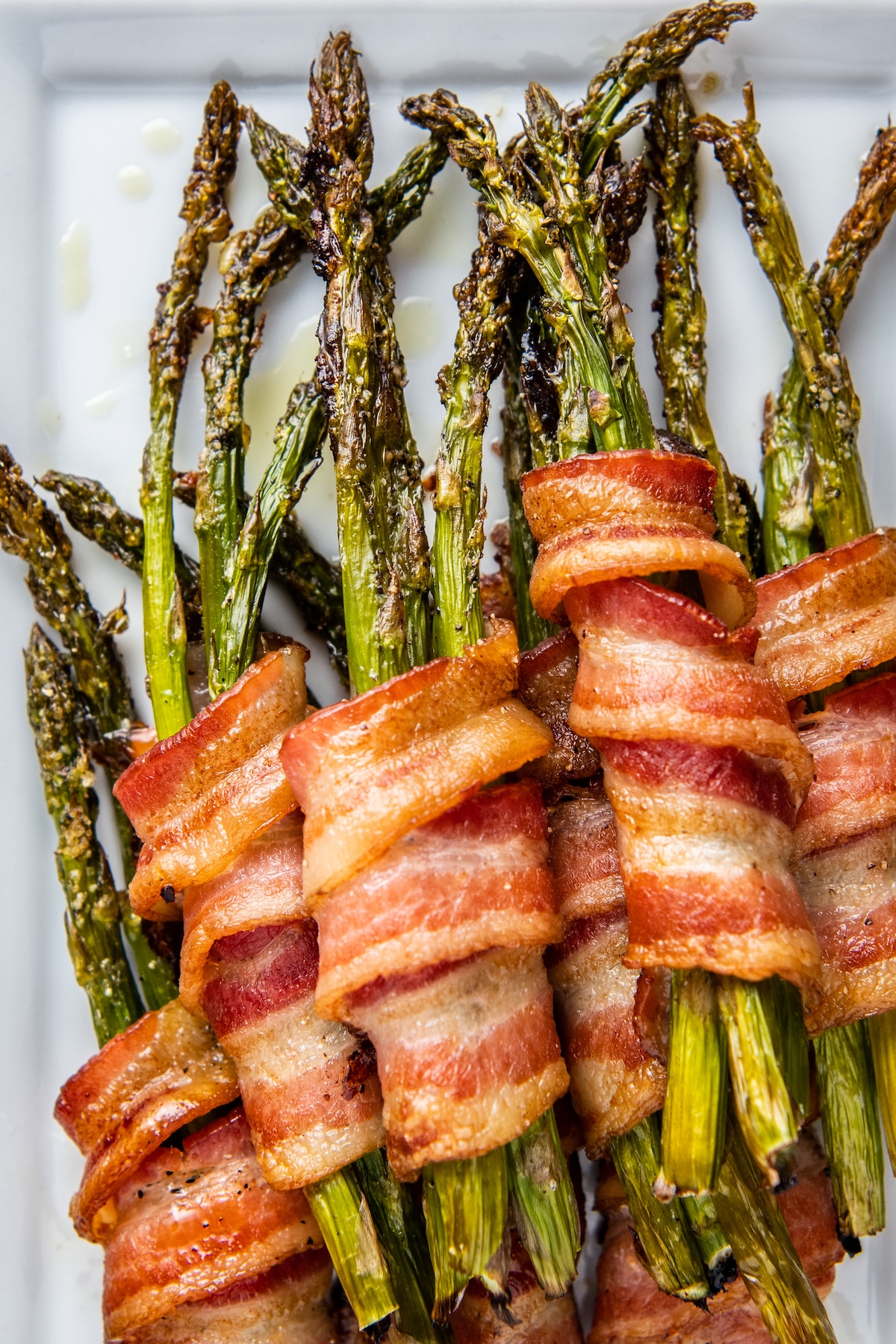 Overhead image of bacon wrapped asparagus stacked on top of each other on a white plate.