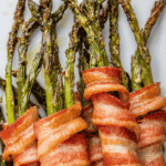 Bacon wrapped asparagus stacked on top of each other on a white plate.