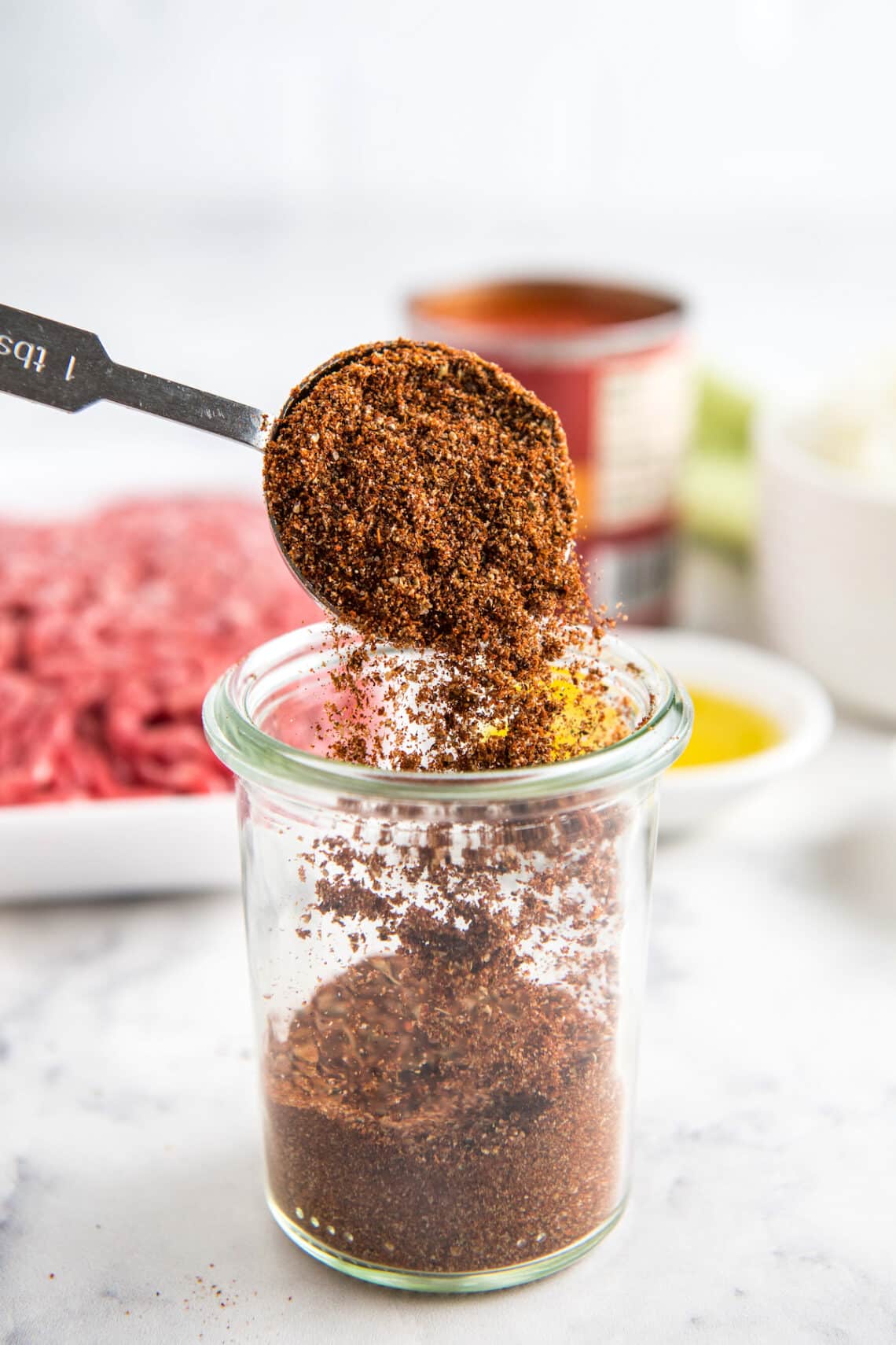 Homemade chili seasoning recipe in a glass jar with a spoon scooping out a serving.
