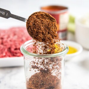 Homemade chili seasoning recipe in a glass jar with a spoon scooping out a serving.