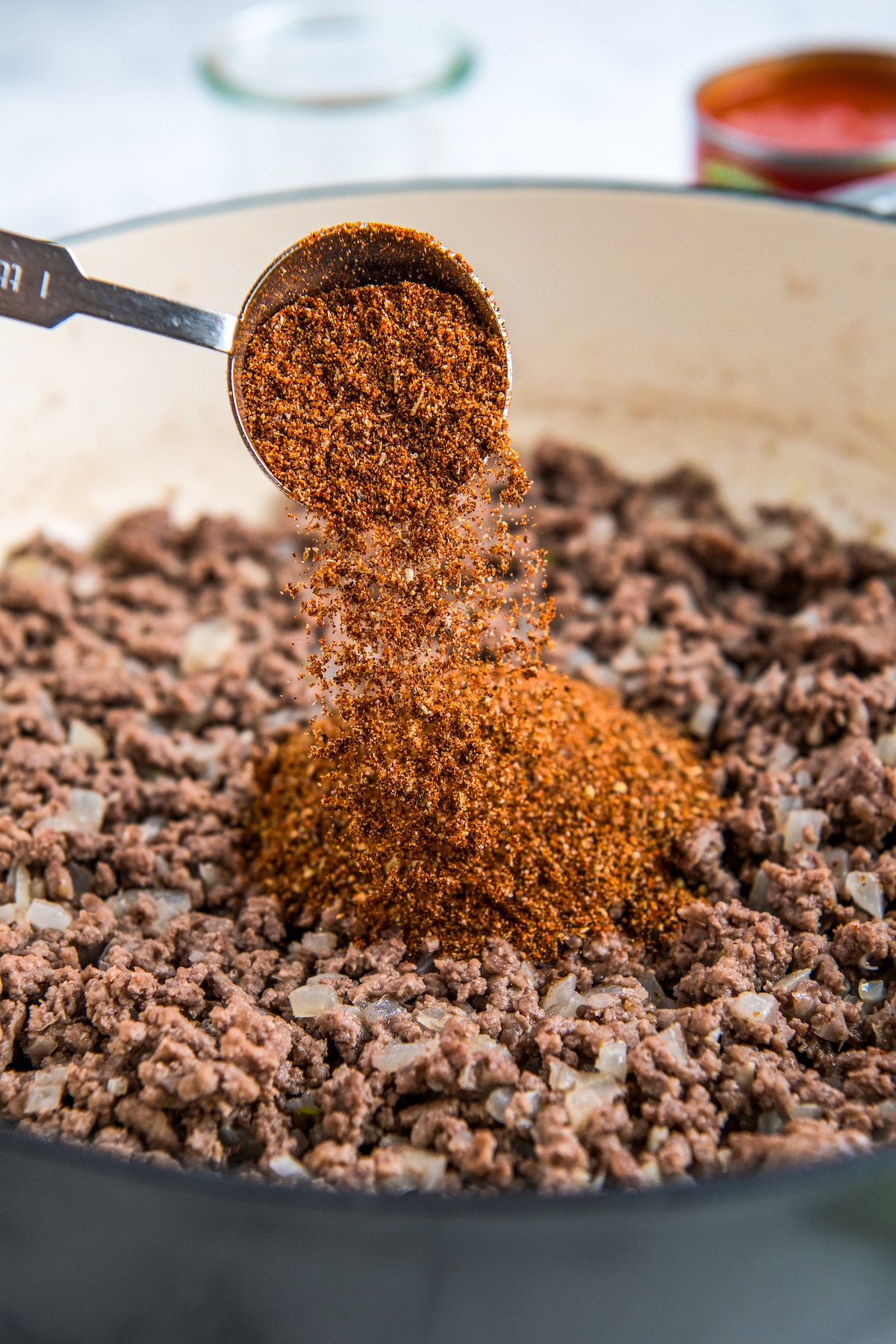 Seasonings being added to a skillet with ground beef and onions.