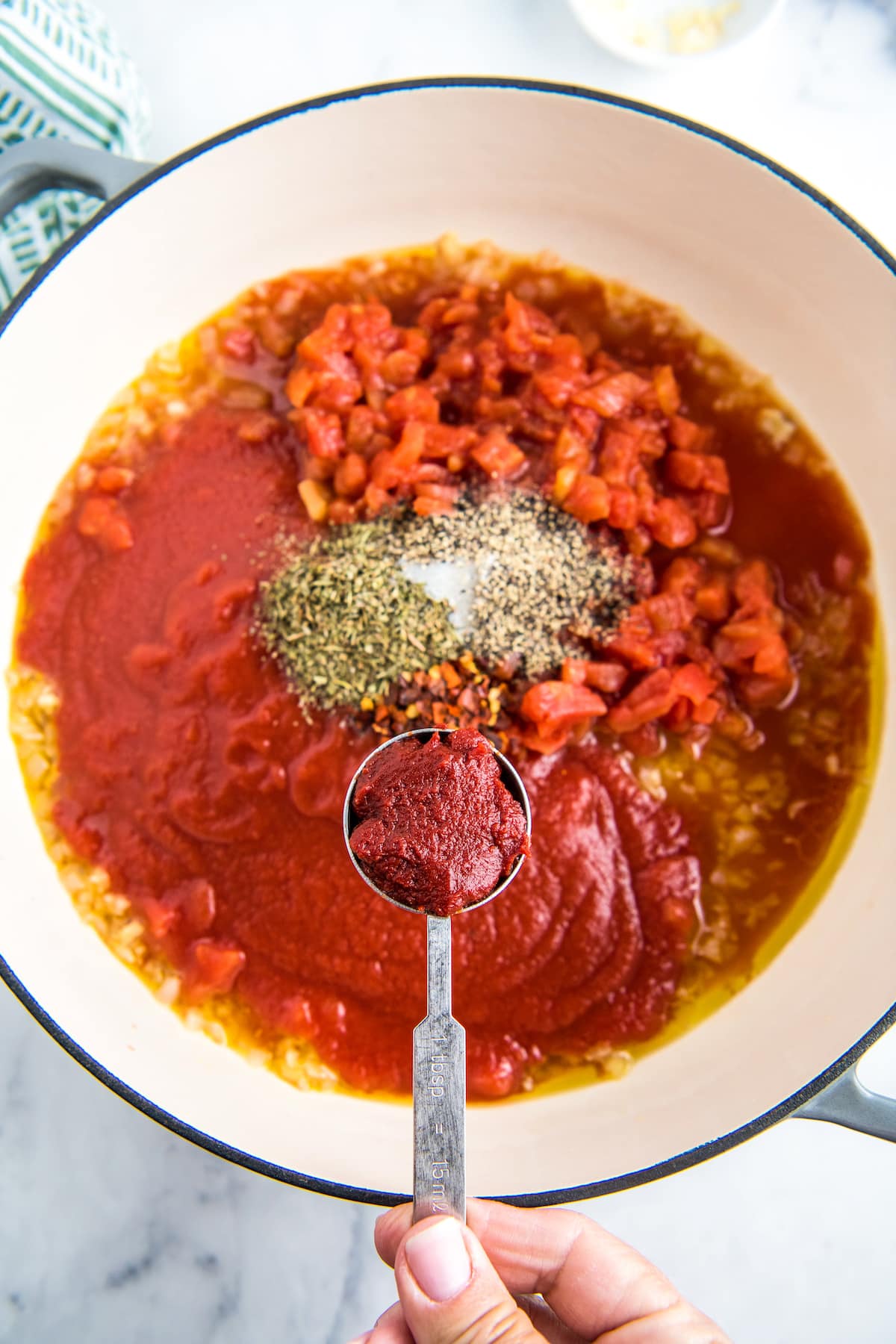 A spoonful of tomato paste being added to a skillet.