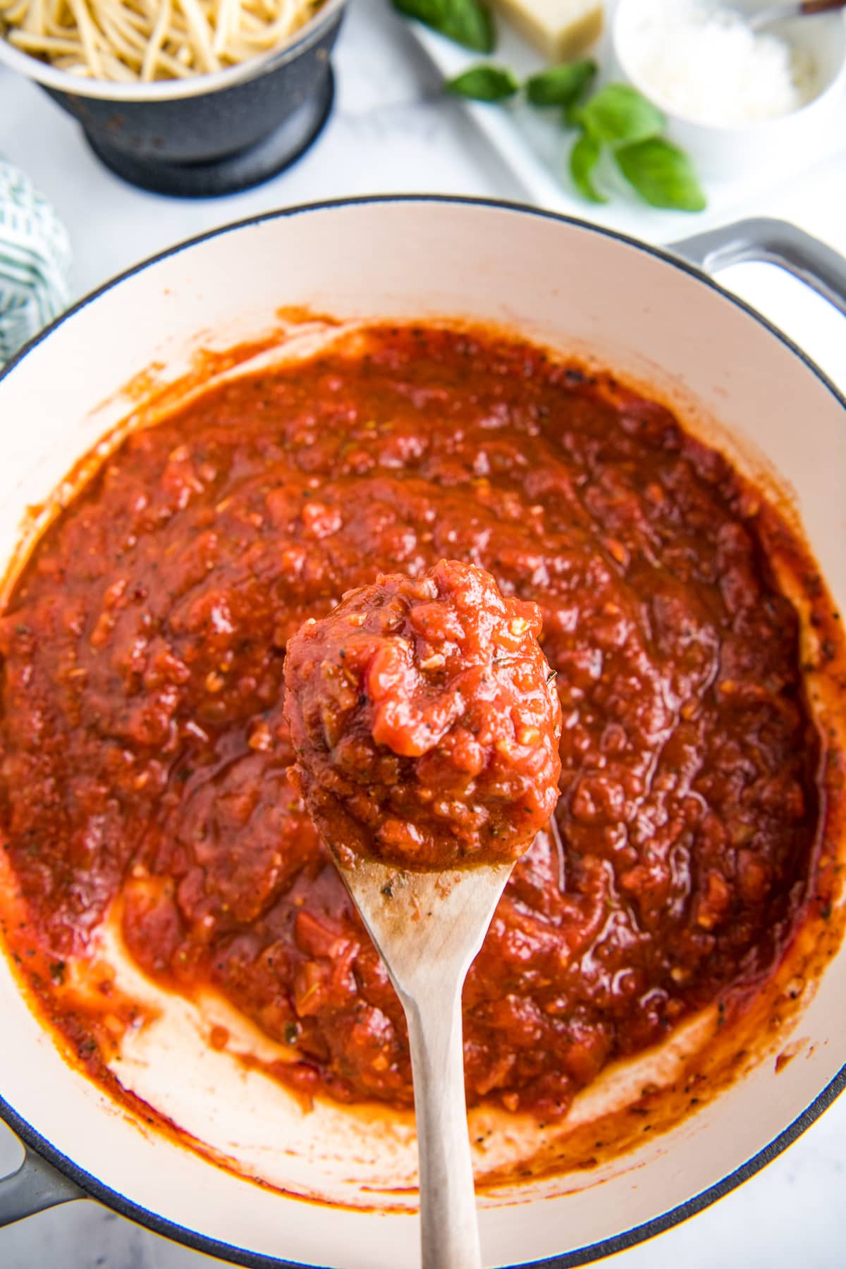 Homemade marinara sauce in a skillet with a wooden spoon scooping up some sauce.