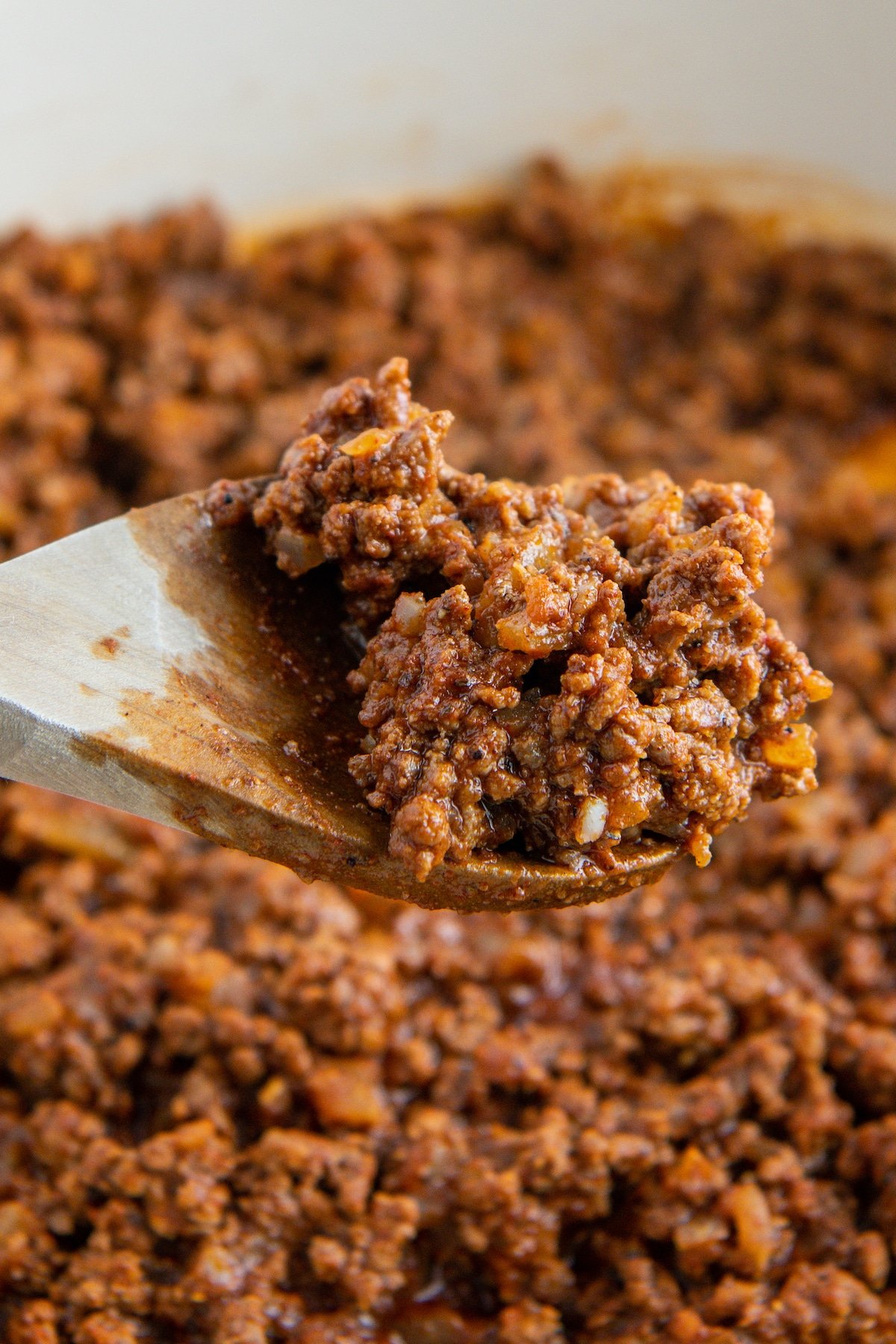 Hot dog chili in a skillet being scooped up on a wooden spoon.