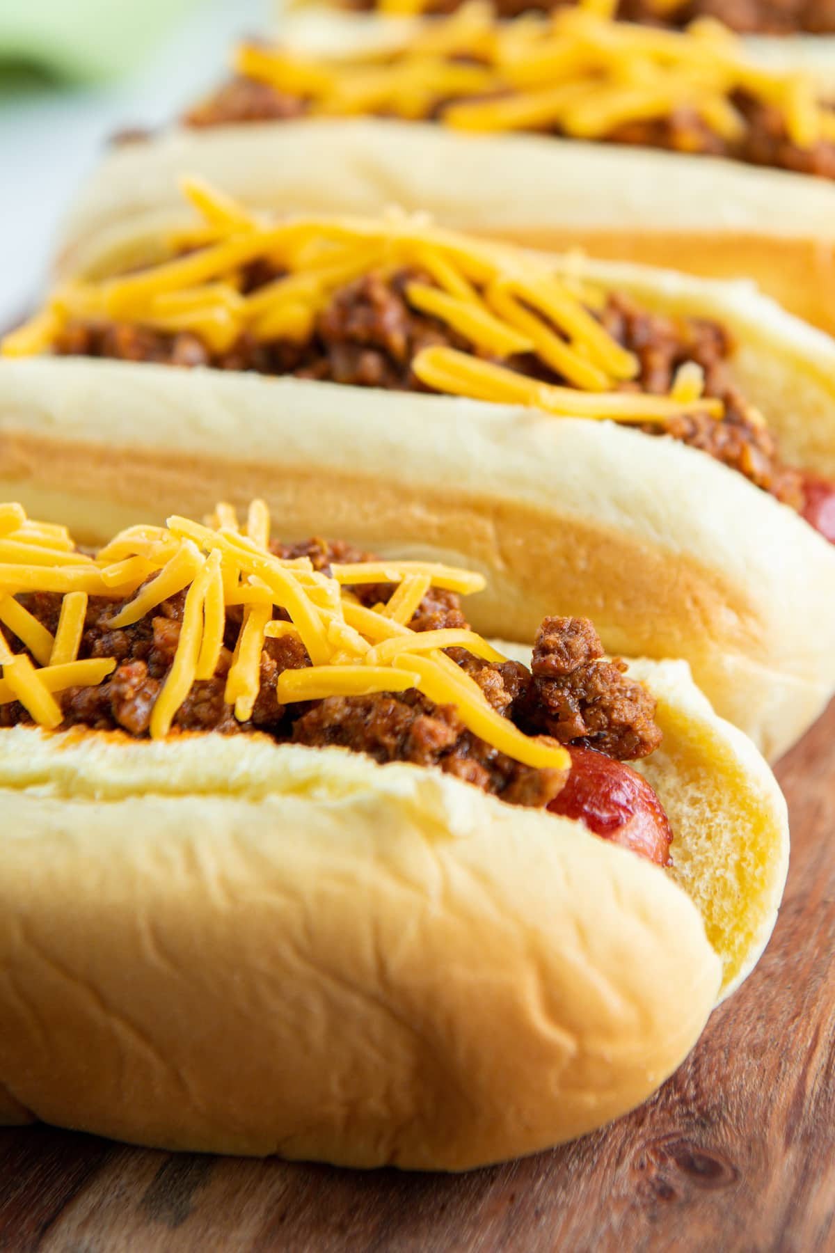 Chili dogs with cheese on top lined up in a row.