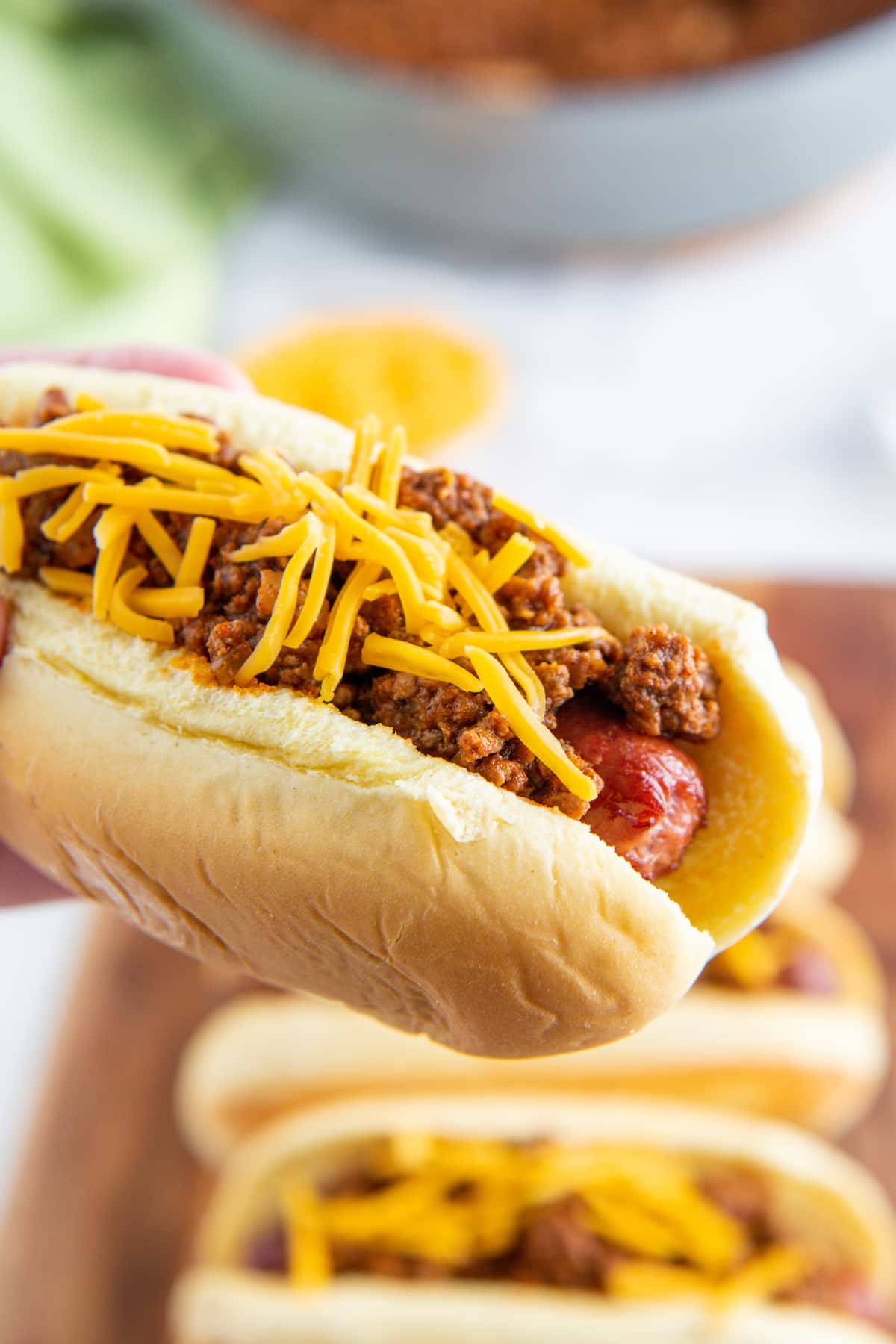A hot dog being held with hot dog chili and cheese on top.