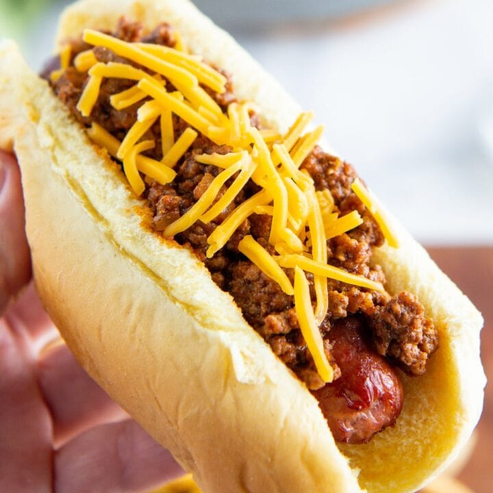 Hot dog chili on top of a hot dog being held in a hand.