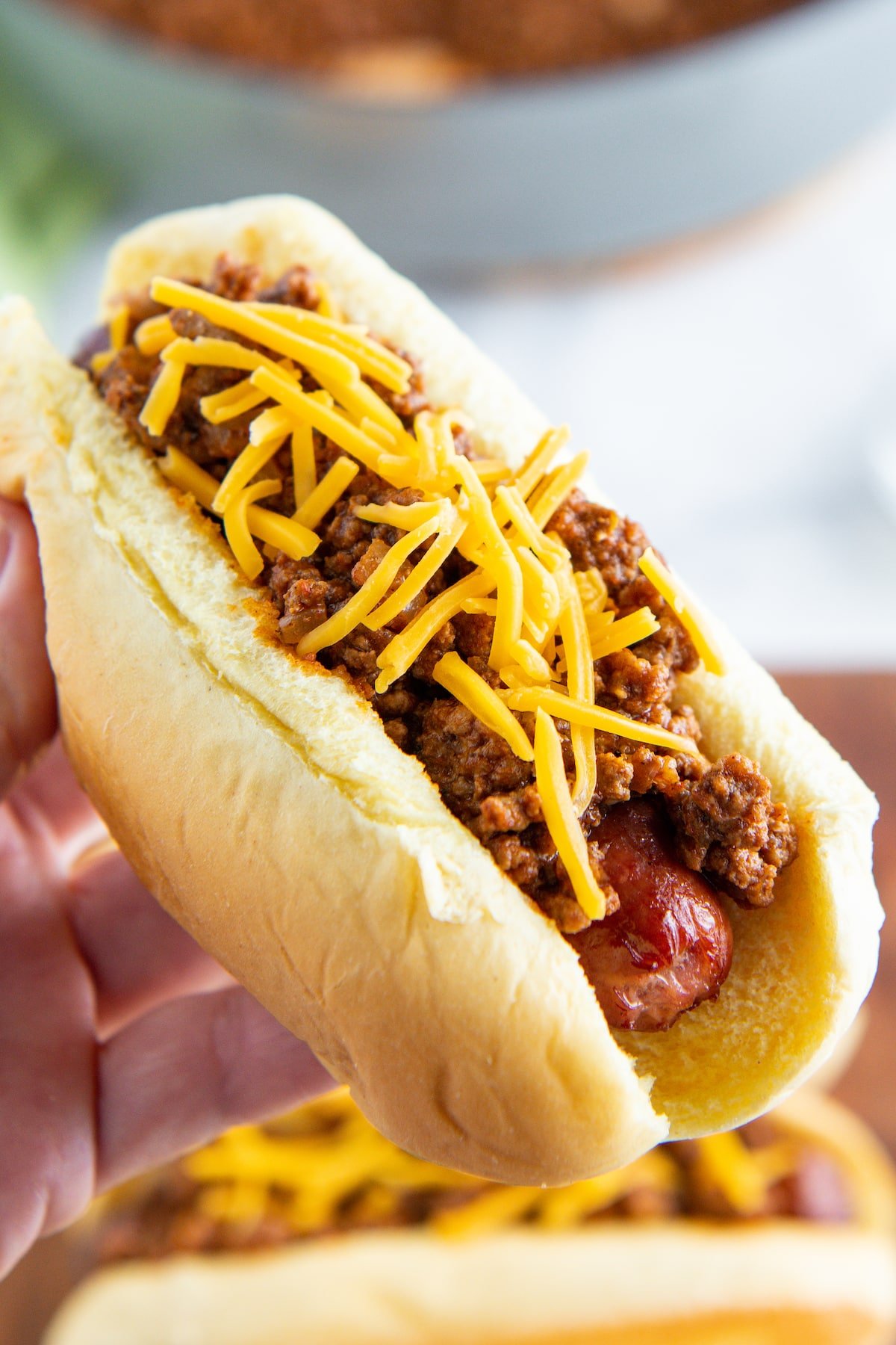 Hot dog chili on top of a hot dog being held in a hand.