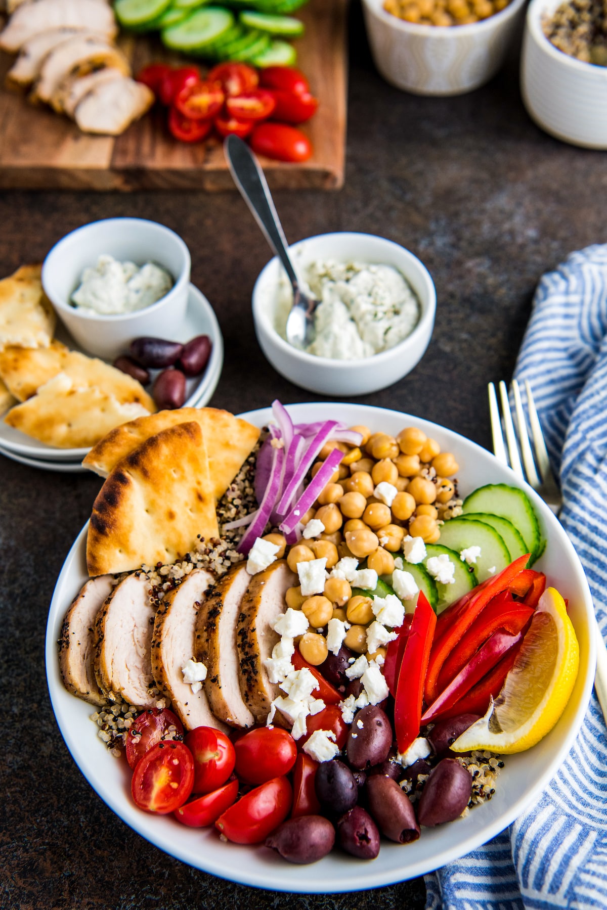 A Mediterranean Quinoa Salad in a white bowl with sides of pita and tzatziki sauce.