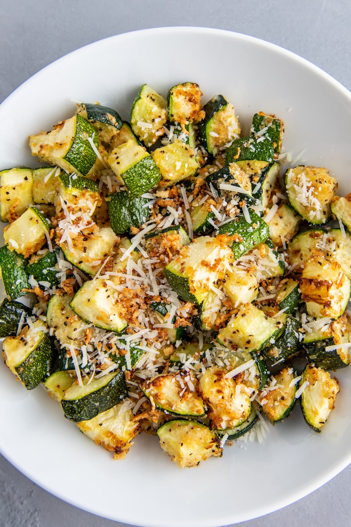A white bowl with air fryer zucchini inside with parmesan cheese sprinkled on top.