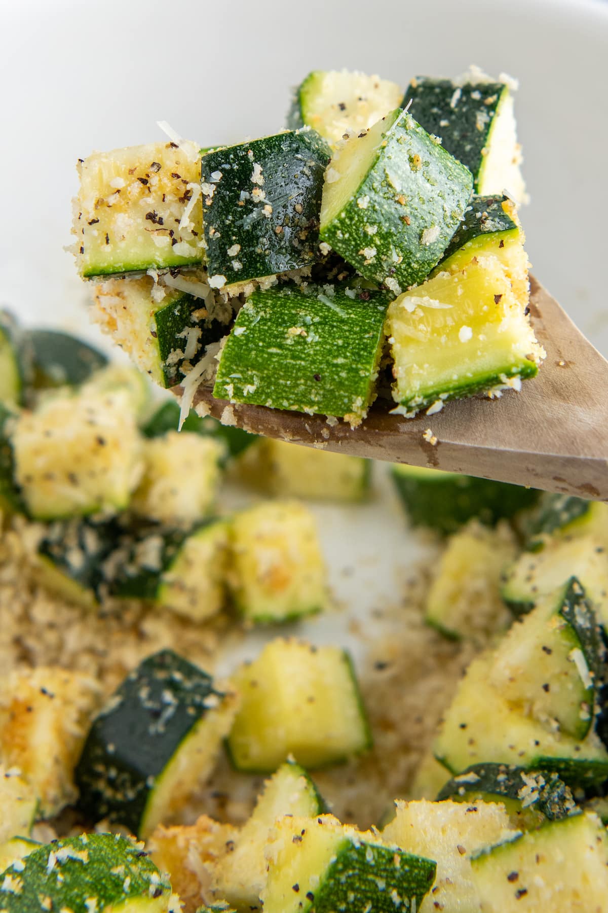 A wooden spoon scooping up zucchini coated in bread crumbs, cheese and spices.