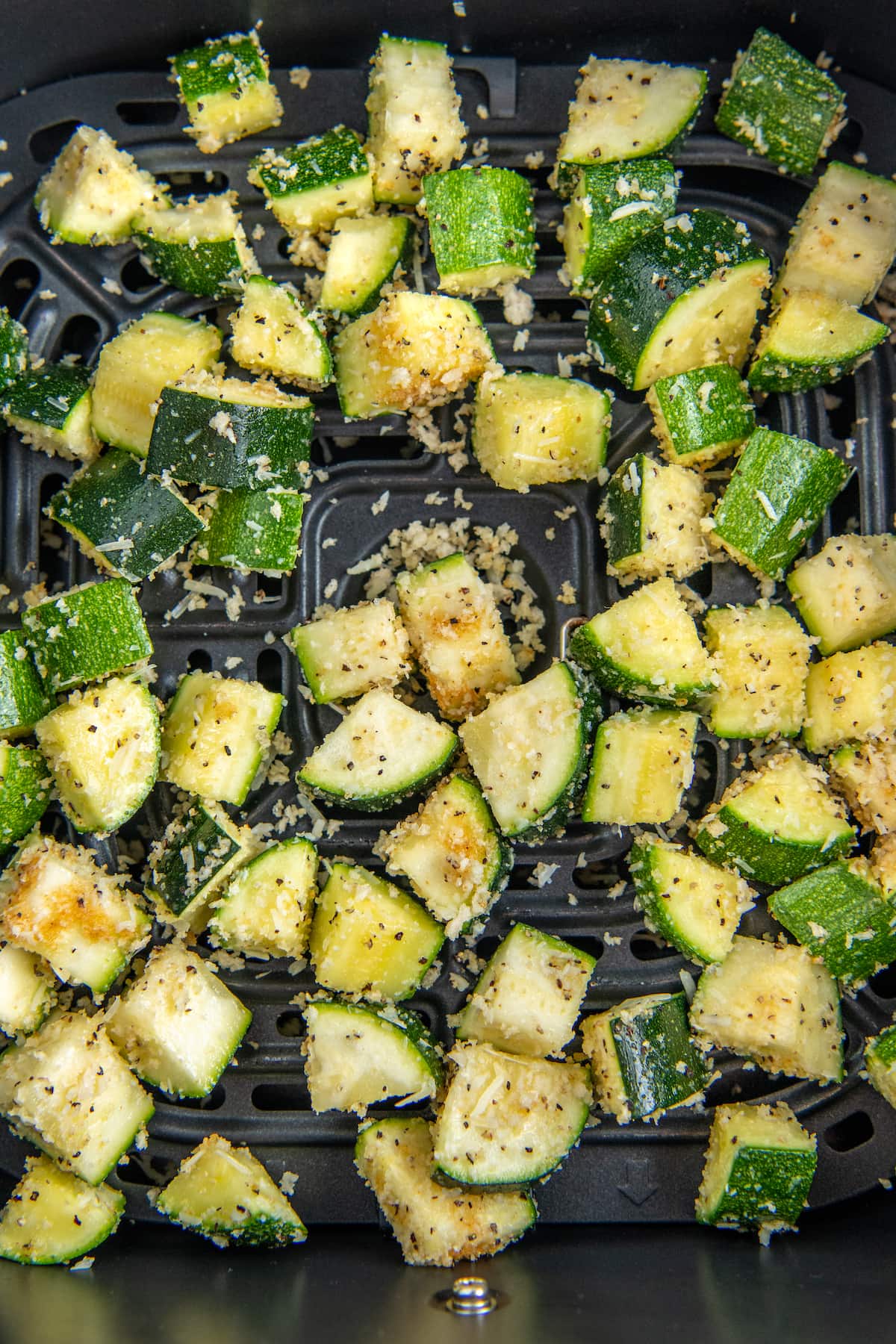 Uncooked zucchini coated in seasonings, cheese and bread crumbs in an air fryer basket.