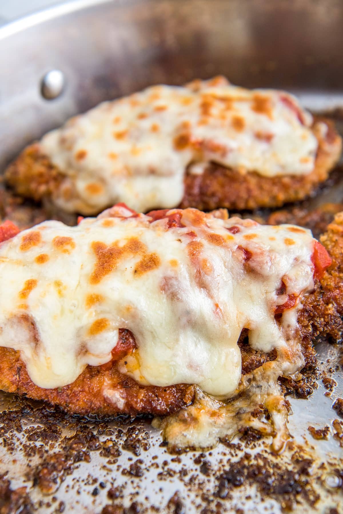 Up close image of chicken parm with melty cheese on top in a skillet.